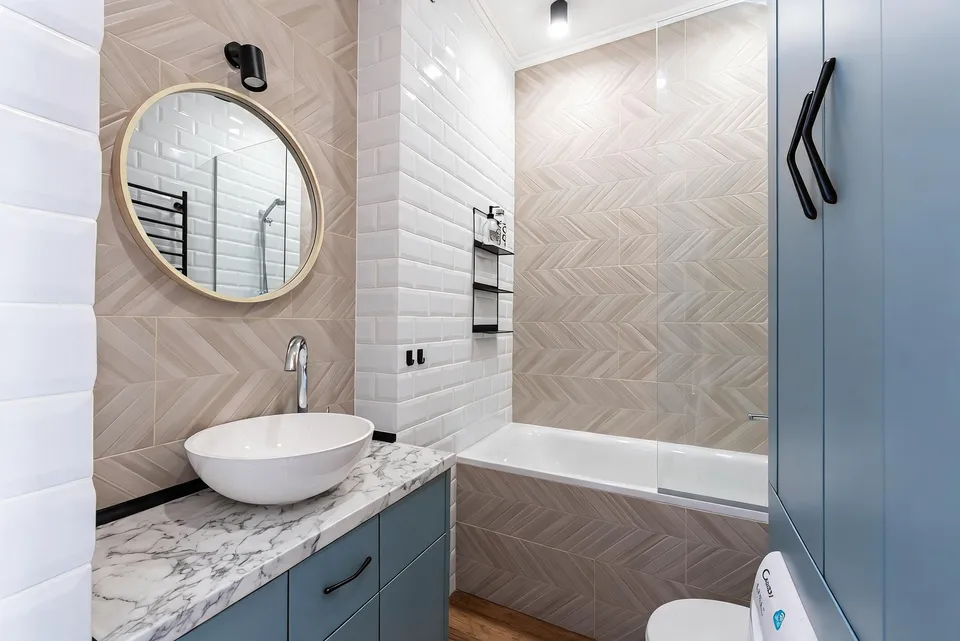 RenderVibe bathroom concept with dusty-blue cabinets and beige herringbone tiles around the white bathtub