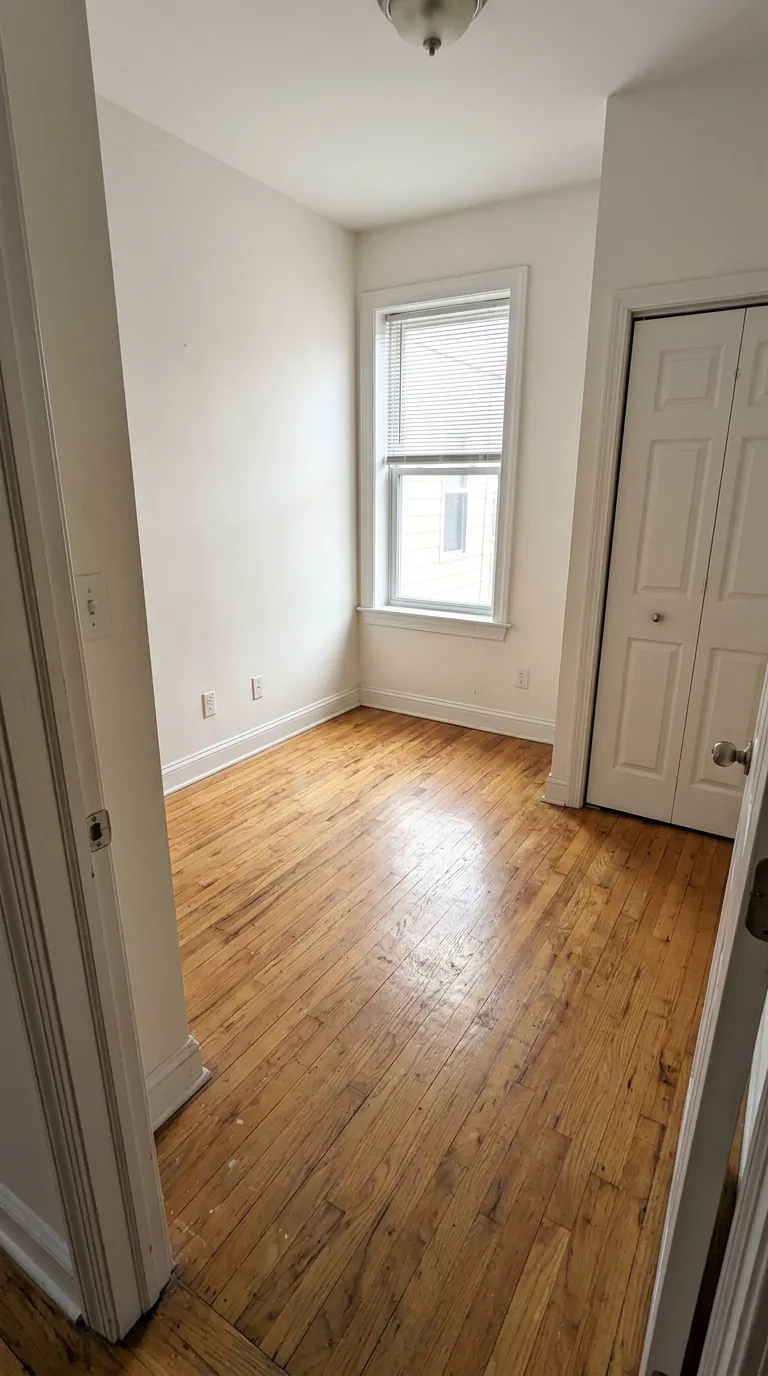 Empty narrow bedroom with a timber floor, window and closet door