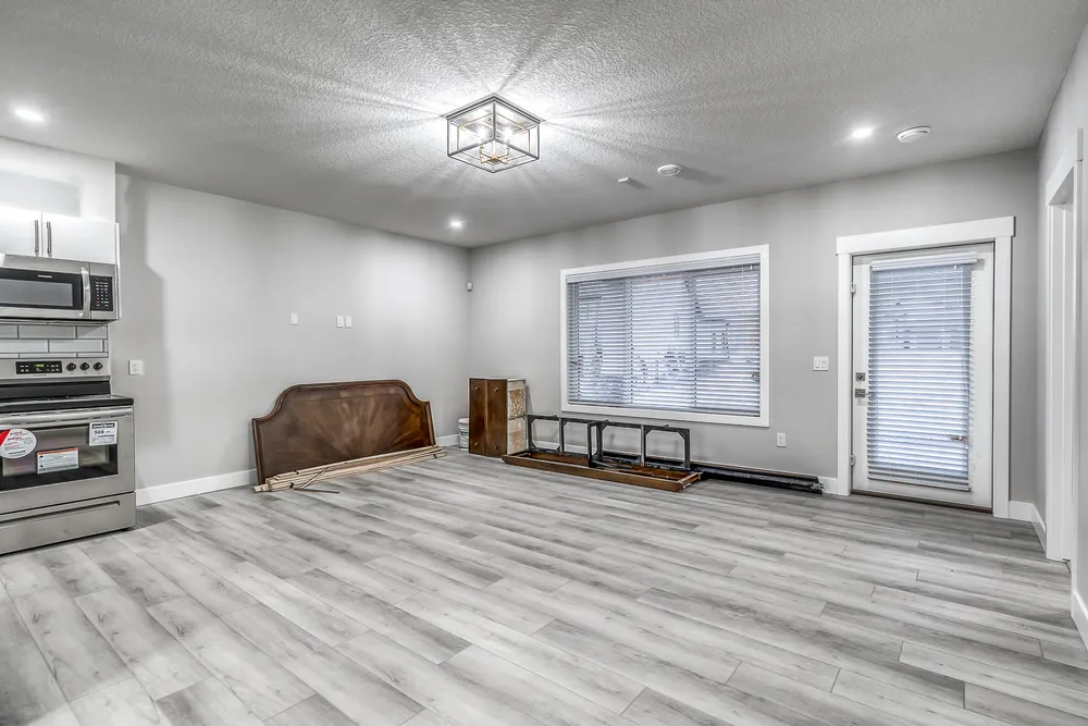 Room with grey flooring, a large window and stored furniture pieces before staging